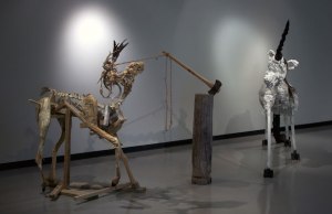 A Stag and Unicorn In the Forest Go  installation approx. 15' X 7' X 6'4” 2013 wood, preserved deer leg, tree trunk, charred tree branch, antlers, axe,  bailing string, bailing wire, coyote ravaged deer skeleton, polyurethane foam,  polystyrene foam, polyurethane adhesive, latex paint, latex acrylic, steel hardware,  chicken wire, concrete, plaster, aluminum fencing wire, horse hair, human hair, goose feathers, gymnasium rope,  tar, machine enamel, spray enamel, oil paint, fabric,  raw hide 