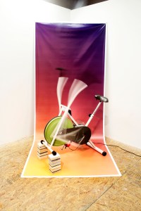 Weslo Pursuit E25 2013 8’x4’x4’ Perpetually running stationary bike, custom printed banner, corian countertop samples Collaborative installation with Corey Dunlap.